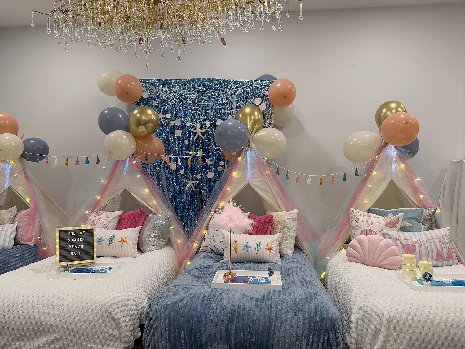 Beach themed sleepover setup with a shimmering teal backdrop, fishing net, starfish, shell pillows and tassel garland